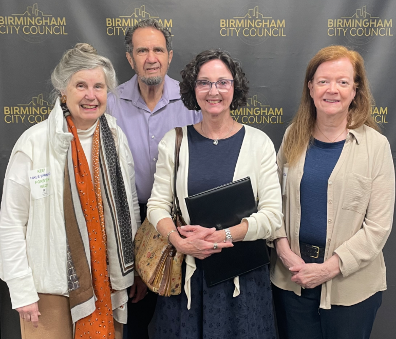 Group of four individuals posing in front of a Birmingham City Council backdrop, smiling and standing together.